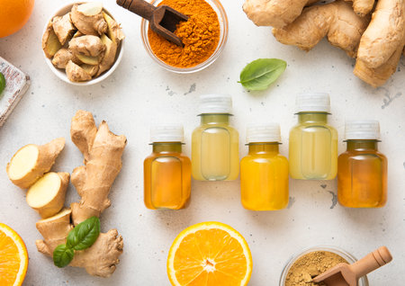 Bottles of immune turmeric ginger energy shot drink with fresh raw ginger roots and oranges fruits on light background.の写真素材