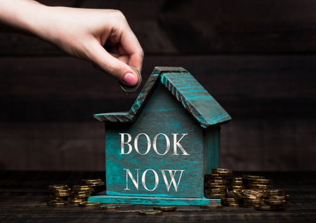 Wooden house model with coins next to it and hand holding the coin with conceptual text.
