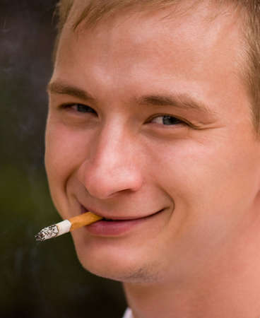 A young man smoking cigarette, focus is set at his faceの写真素材