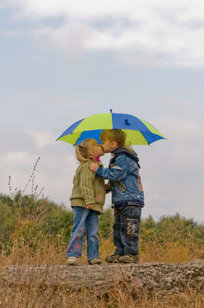 Little boy kiss girl, under umbrella in autumn dayの写真素材