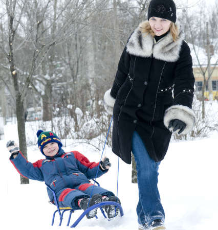 Mother pulling son on sledge, bright and white winter sceneの写真素材