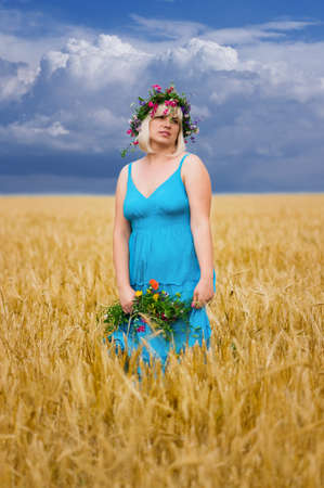Beautiful woman in wreath of wild flowers in wheat meadow on sunny dayの写真素材