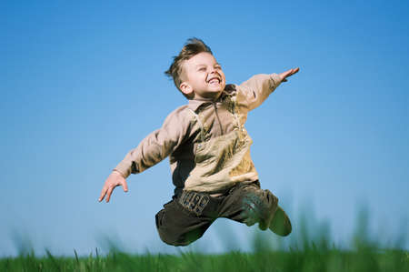 Happy little boy jumping in field against blue skyの写真素材