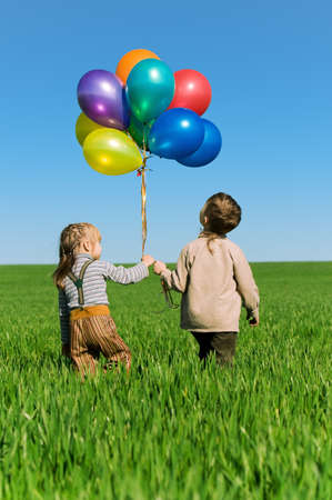 Happy sister and brother with balloons walking on the spring fieldの写真素材