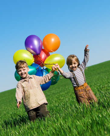 Happy sister and brother with balloons walking on the spring fieldの写真素材