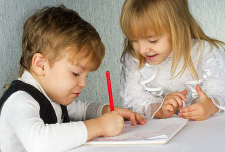 Beautiful little girl and boy is drawing with pencils on paperの写真素材