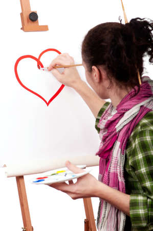 Girl with paint brush near easel, painting red heart on canvas.の写真素材