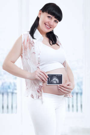 Beautiful pregnant woman is holding her stomach and a photo of her Ultrasound