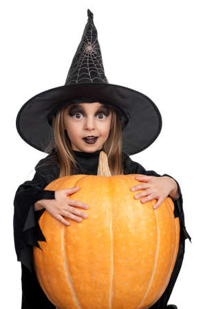 Portrait of little girl in black hat and black clothing with pumpkin on white backgroundの写真素材