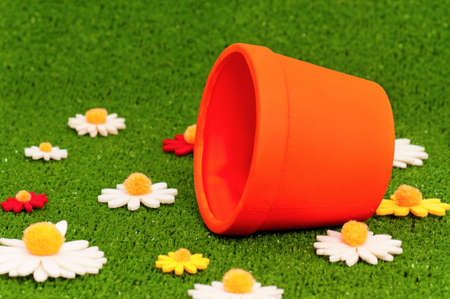 Small orange flowerpot on artificial green grass with flowersの写真素材