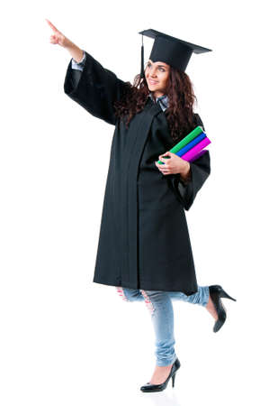 Young graduate girl student in mantle with books showing something, isolated on white backgroundの写真素材