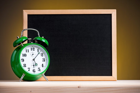 Big green alarm clock with blackboard on dark yellow background