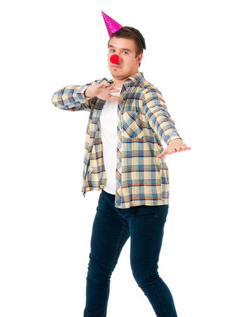 Young man in shirt with red clown nose and birthday cap, isolated on white backgroundの写真素材