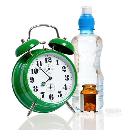 Big green alarm clock with bottle of water and pills, isolated on white backgroundの写真素材
