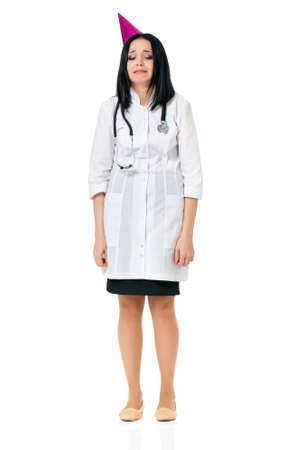 Unhappy young female doctor wearing birthday cap, isolated white backgroundの写真素材