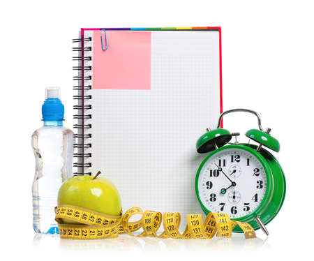 Green alarm clock, apple, bottle of water and measuring tape with blank notebook as concept of diet - isolated on whiteの写真素材