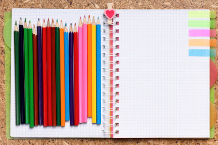 Notepad and colour pencils against wooden surface, top view