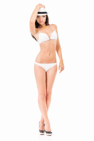 Sexy young brunette woman posing in a white bikini and hat, isolated on white backgroundの写真素材