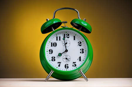 Big green alarm clock on dark yellow backgroundの写真素材