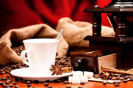 Coffee grinder and cup of coffee with spices on dark red backgroundの写真素材