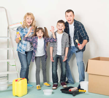 Cheerful family makes repairs at home. Happy mother, father, son and daughter - painting wall at roomの写真素材