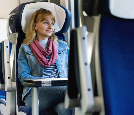 Young woman traveler sitting in train, looking through windowの写真素材