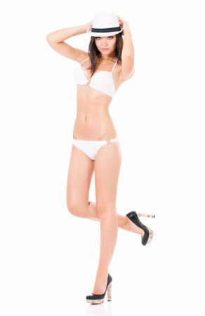 Sexy young brunette woman posing in a white bikini and hat, isolated on white backgroundの写真素材