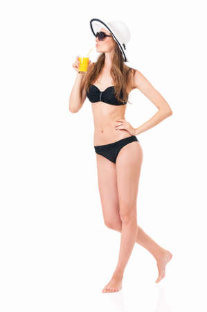 Prett girl posing in bikini summer hat and sunglasses, drink orange juice, isolated on white backgroundの写真素材