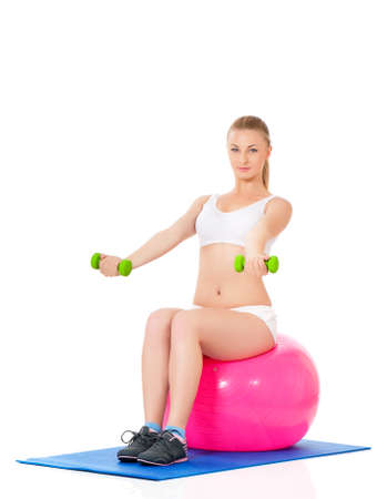 Beautiful young girl doing exercises with fit ball and dumbbells isolated over white backgroundの写真素材