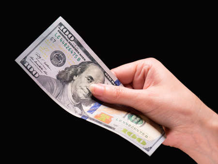 Close up of female hand holding money - US dollar banknotes against dark backgroundの写真素材