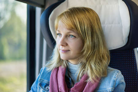 Young pretty woman traveler sitting by train or bus, looking through windowの写真素材