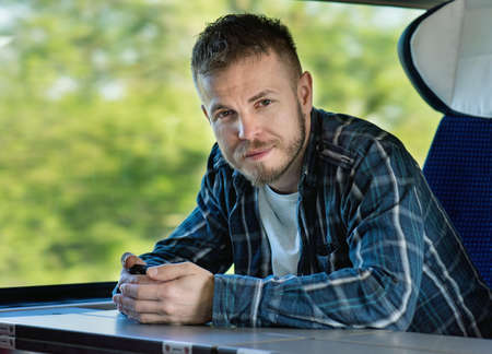 Young man traveler in a train or bus with mobile phone, looking at camera.の写真素材