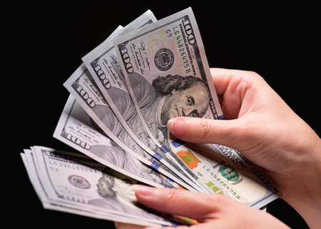Close up of female hand holding money - US dollar banknotes against dark backgroundの写真素材