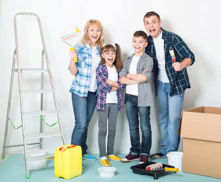 Cheerful family makes repairs at home. Happy mother, father, son and daughter - painting wall at roomの写真素材