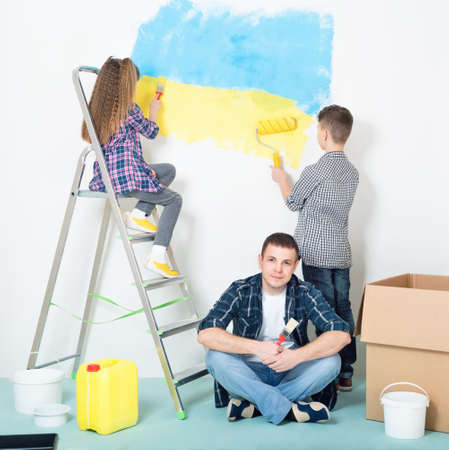 Happy family - children and father, makes repairs at home - painting big Ukrainian flag on wall at home.の写真素材