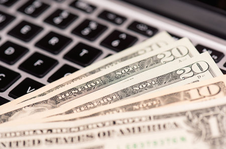 Workplace with money and notebook - US dollar banknotes on keyboard of laptop computer.