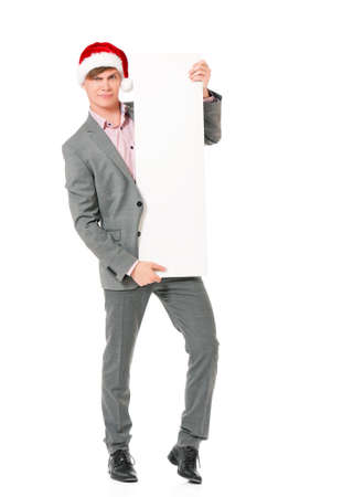 Caucasian man wearing christmas hat for santa. Young businessman in gray suit with blank sign isolated on white background. Successful boy wearing Santa Claus hat - full lenght portrait.の写真素材