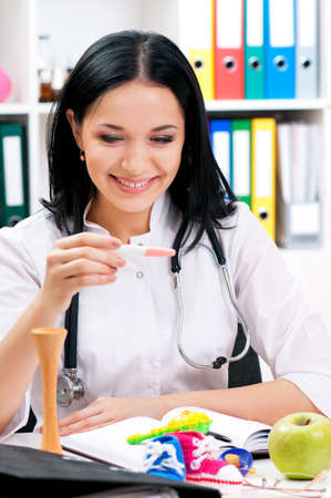 Smiling medical nurse with holding positive pregnacy test. Portrait of happy young doctor at office. Beautiful young woman doctor sitting at the desk in hospital.の写真素材