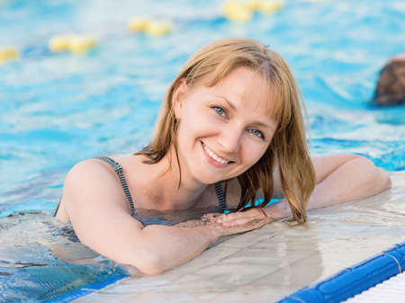 Smiling beautiful young woman in the swimming pool at aquapark. Portrait of a happy girl having fun enjoyable time on vacation. Looking at camera.の写真素材