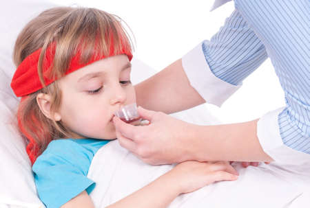 Mother giving her daughter cough syrup at home. Sick little girl in bed taking medicine with plastic cup.の写真素材