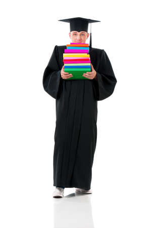 Male student carrying heavy books. Full length portrait of a young graduation man in mantle holding stack of books isolated on white background.の写真素材