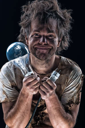 Portrait of burnt man with light bulb and electric plug over black background. Young man with dirty burnt face in funny sad expression in electricity DIY has a electric shock. の写真素材
