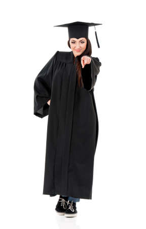 Beautiful graduate girl student in mantle pointing at camera choosing you, isolated on white backgroundの写真素材