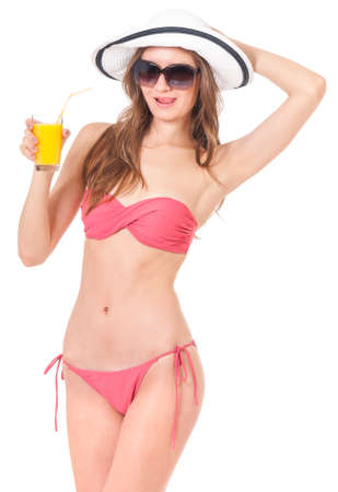 Pretty girl posing in bikini summer hat and sunglasses, drink orange juice, isolated on white backgroundの写真素材