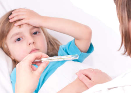 Sick little girl in bed. Mother or doctor with thermometer is sitting near the bed. Focus on thermometer.の写真素材