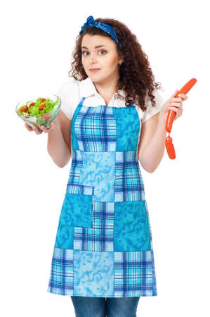 Beautiful young woman choosing between fresh salad and sausagesの写真素材