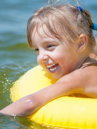 Portrait of little smiling girl with inflatable rubber circle in the sea in sunny day. Summer vacations concept.の写真素材