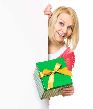 Portrait of happy smiling young woman, showing empty blank signboard with copyspace. Businesswoman holding gift box and peeping behind blank board, isolated on white background.の写真素材