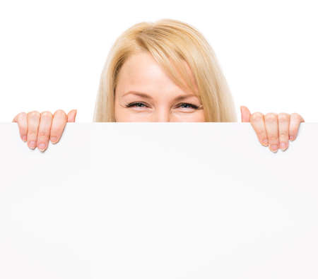 Young woman with surprised eyes peeking out from behind billboard paper poster. Businesswoman holding big white banner, isolated on white background.の写真素材