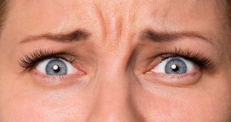 Close-up scared face of beautiful young woman with beautiful blue eyes and big pretty eyelashes and eyebrows. Macro of human eyes - surprise or shock, looking at camera.の写真素材